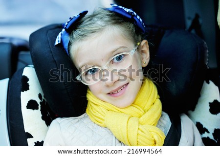 Beauty school aged kid girl in glasses and yellow scarf in the car seat with belt