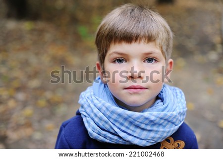 Portrait of adorable and fashionable little boy with big blue eyes in blue coat and scarf outdoor at the nice autumn day