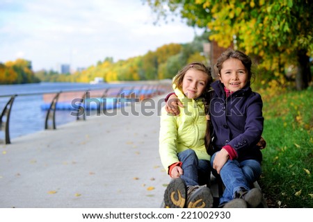 Two adorable school aged tween girls friends having fun in the autumn park, smiling, look into the camera on a beauty autumn day
