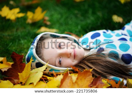 Happy little child girl lying on the grass and yellow maple leaves in autumn park