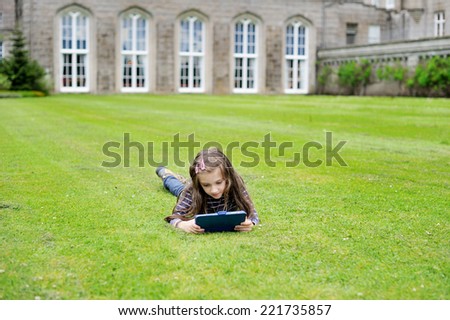 Adorable school aged girl on the lawn reading  travel guide during sightseeing on family vacation