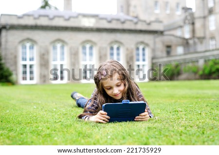 Adorable school aged girl on the lawn reading  travel guide during sightseeing on family vacation