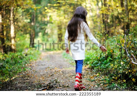 Beauty school aged brunette girl in white sweater and rain boots in the beauty autumn forest. View from the back.