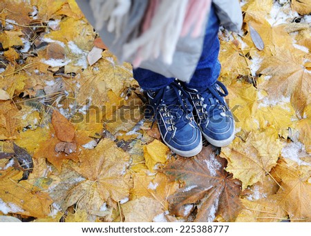 Blue kid girl boots on the yellow mapple leaves with first snow on it