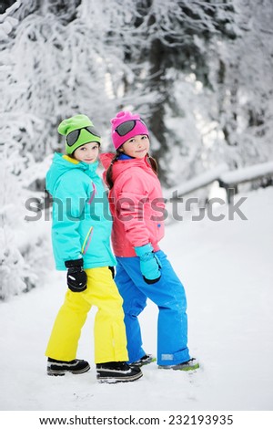 Two adorable kid girls in warm colorful clothes walking in the snowy park on beauty winter day