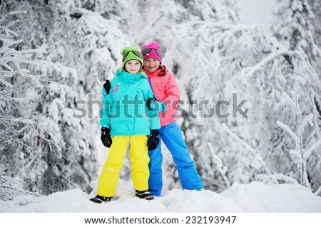 Two adorable kid girls in warm colorful clothes walking in the snowy park on beauty winter day