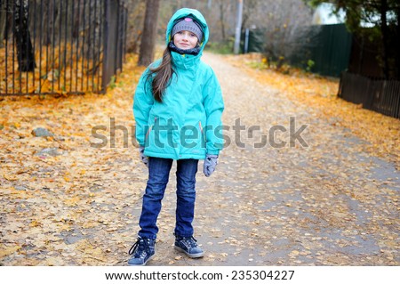 Cute child girl in jeans and colorful jacket walking in snowy winter park