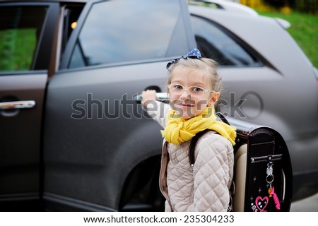 Beauty school aged kid girl in glasses and yellow scarf near the car