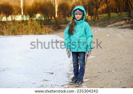 Cute child girl in jeans and colorful jacket walking in snowy winter park