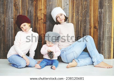 Cute kid girls of 10 month, 7 and 12 years old wearing knitted trendy winter hats and sweaters posing over wood wall