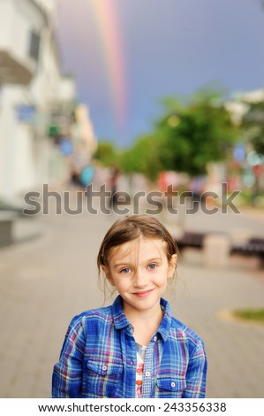 Adorable kid girl in the fancy clothes on the real rainbow background in the city street