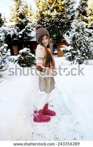 Adorable little girl, beauty school aged in a pastel colors  knitted sweater, gold skirt, fur vest and brown hat, playing in snow, having fun outdoors in a beautiful sunny  winter park