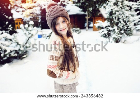 Adorable little girl, beauty school aged in a pastel colors  knitted sweater, gold skirt, fur vest and brown hat, playing in snow, having fun outdoors in a beautiful sunny  winter park
