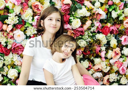 Two beauty smilling  school aged girls in dresses over flower wall