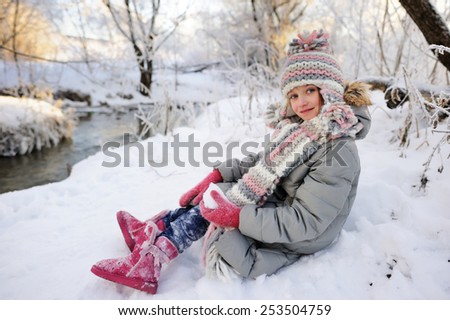 Adorable little girl,  in a knitted hat and gray down coat, playing  outdoors in a beautiful winter park