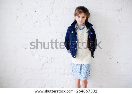 Little fashion girl in fashion  clothes posing over white brick background