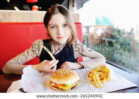 Cute little  girl in school uniform  eating a hamburger and potatoes in the restaurant