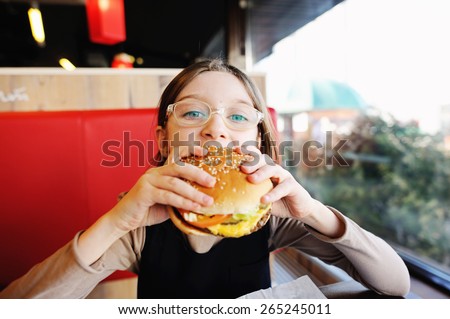 Cute little  girl in glasses and school uniform  eating a hamburger and potatoes in the restaurant