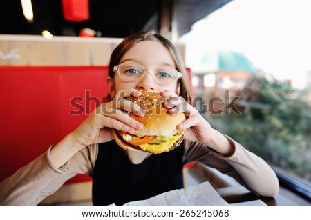 Cute little  girl in glasses and school uniform  eating a hamburger and potatoes in the restaurant