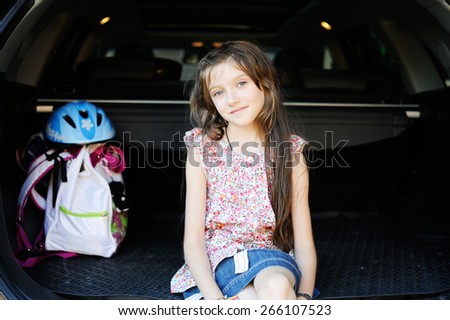 a little girl sitting in the car with backpack and helmet