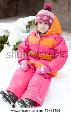 Beauty toddler girl in pink winter hat and snow suit sitting on the snow