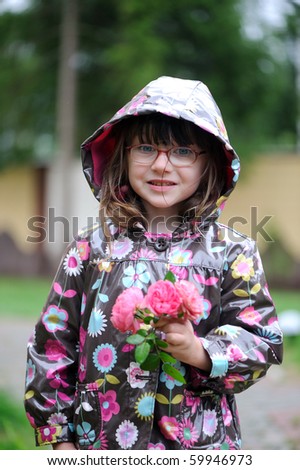 Adorable small girl in  glasses in colorful rain coat with roses