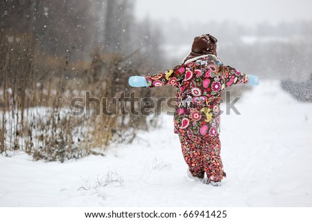 Small girl in colorful snowsiut plays with snow in strong snowfall