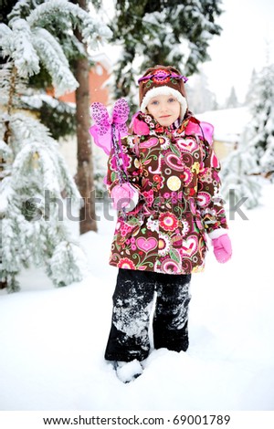 Adorable little girl in colorful snow suit and hat with fairy wing and magic wand plays outside in snowfall