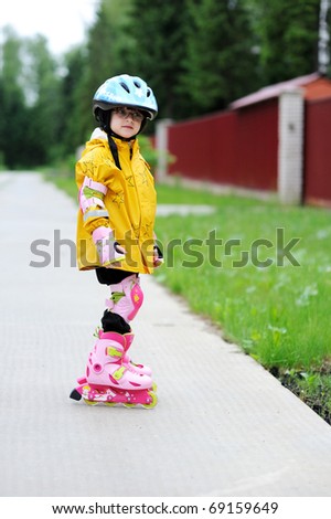 Adorable little girl in yellow raincoat, blue helmet and pink roller-skates