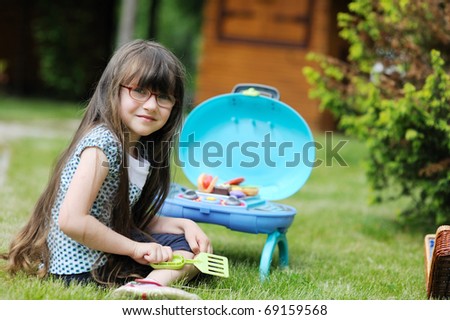 Adorable little girl with long dark hair plays with her toy BBQ set  on the back yard