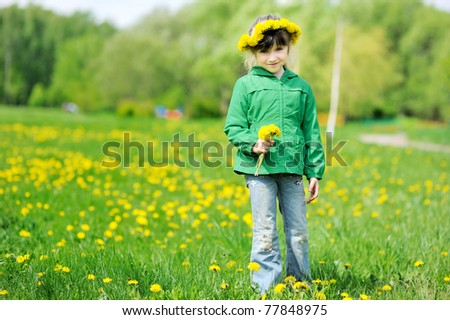 Adorable little girl with long dark hair and dandelions wreath on yellow dandelions field