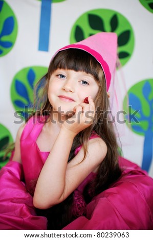 Beauty little princess in pink dress and pink fairy hat with long brunette hair and big blue eyes with raspberry on funny background