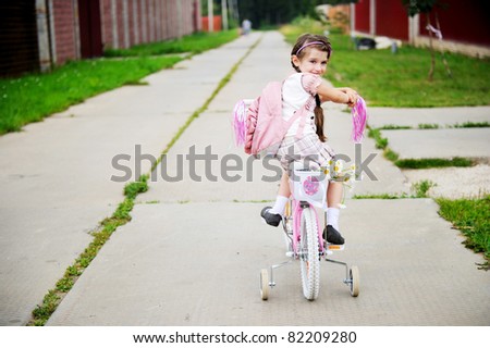 Young school girl with backpack rides her pink bike to school