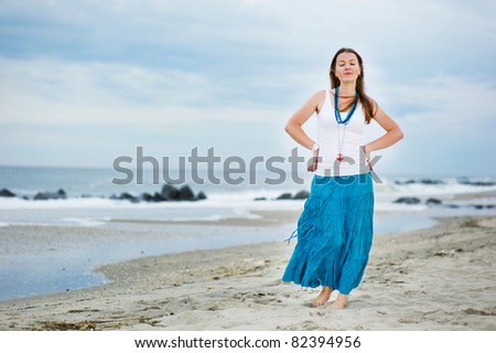 Beautiful brunette woman in white cami and turquoise skirt dreams with her eyes closed against the ocean background