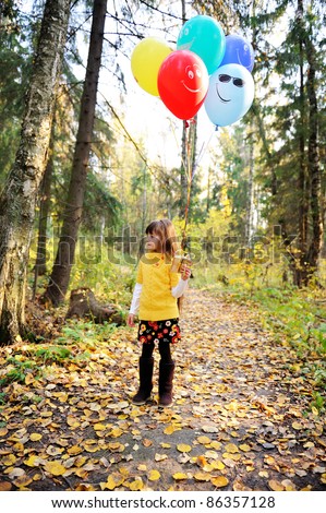 Child girl with colorful balloons walking alone in autumn forest