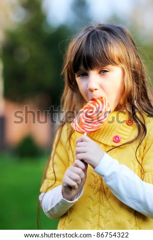 Portrait of cute little girl eating big lollipop on a stick outdoors