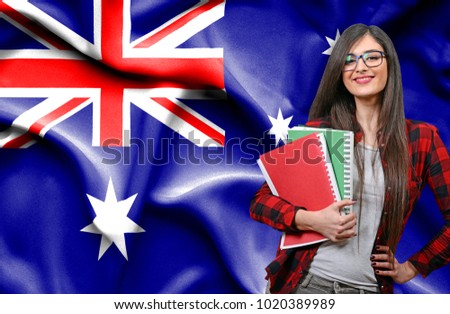 Happy female student holdimg books against national flag of Australia