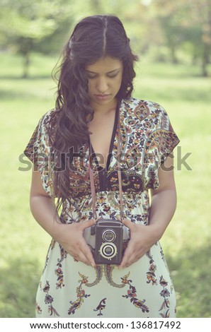 Retro image of beautiful woman holding vintage camera outdoors