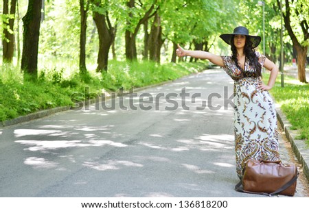 Beautiful young woman hitchhiking along a road
