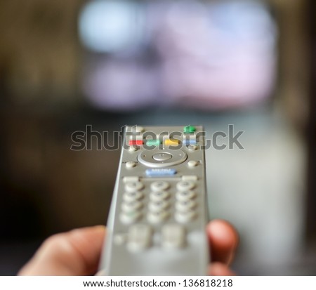 Hand holding remote controller with tv in the background