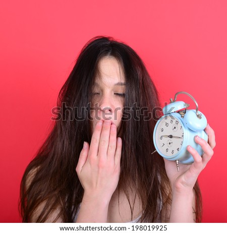 Portrait of sleepy young female in chaos holding clock against red background - Running late concept