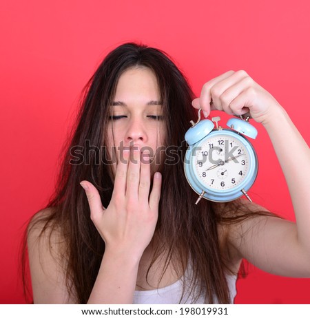 Portrait of sleepy young female in chaos holding clock against red background - Running late concept