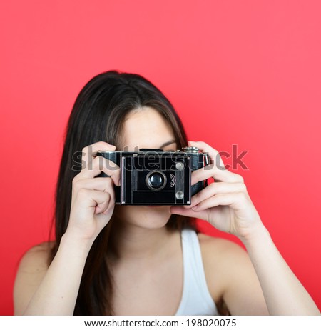 Portrait of young female holding vintage camera against red background with focus on camera