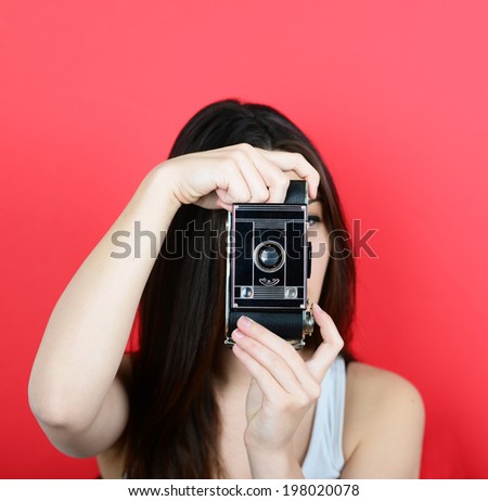 Portrait of young female holding vintage camera against red background with focus on camera