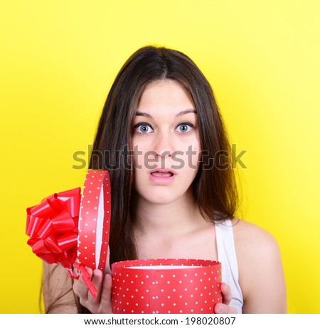 Portrait of happy woman opening gift box against yellow background