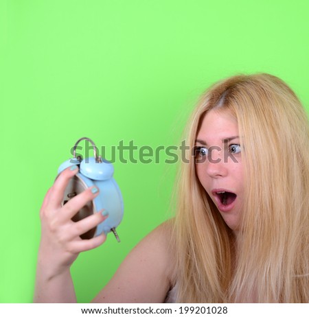 Portrait of sleepy young female in chaos holding clock against green background - Running late concept