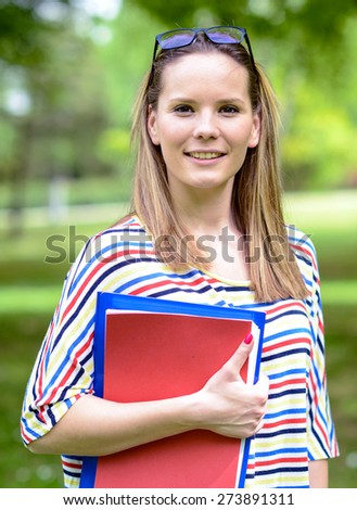 Young happy student woman with the book in her hands is standing and smiling in the university park