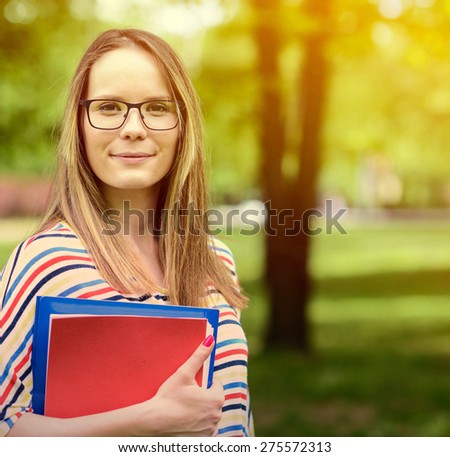 Young happy student woman with the book in her hands is standing and smiling in the university park