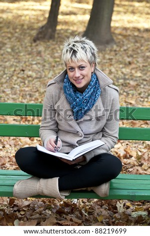 Portrait of young attractive smiling woman sitting on park bench and learning