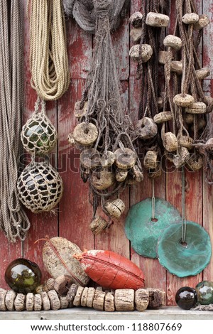 Old fishing equipment: glass floats, fishing nets and rounded stone sinkers hanging at a boathouse wall in Norway.